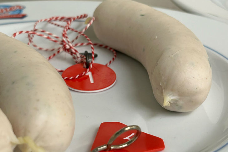 zwei zusammenh&auml;ngende W&uuml;rste mit der Pr&uuml;fnummer verknotet und in einem Top aus Salzwasser auf 70 Grad Celsius erhitzt